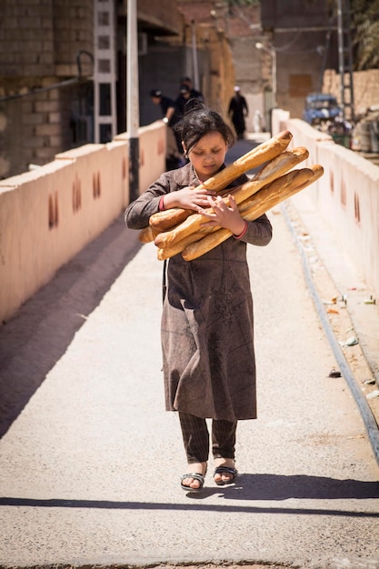 Giovane ragazza che attraversa il ponte con baguette piene di braccia nelle sue mani nella città di Ghardaia, nella valle di M'Zab