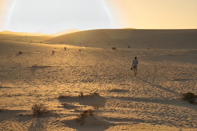 Giovane ragazza che cammina verso il sole sulle dune di Corralejo a Fuerteventura in un tramonto incredibile