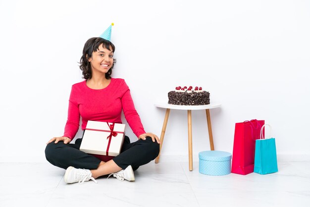 Giovane ragazza che festeggia il suo compleanno seduta sul pavimento isolato su sfondo bianco con le braccia incrociate e guardando avanti