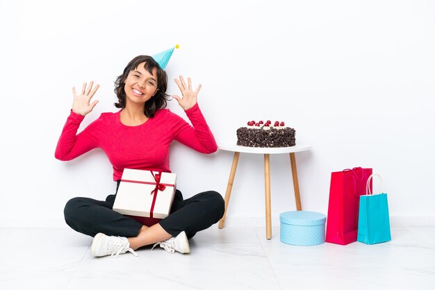 Giovane ragazza che festeggia il suo compleanno seduta sul pavimento isolato su sfondo bianco contando dieci con le dita