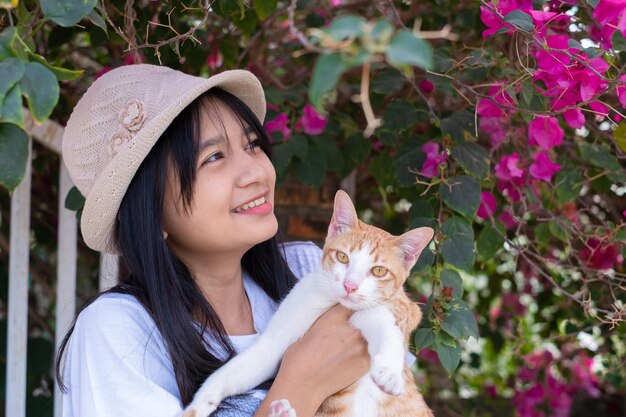 Giovane ragazza che gioca con un gatto in piedi sotto l'albero dei fiori