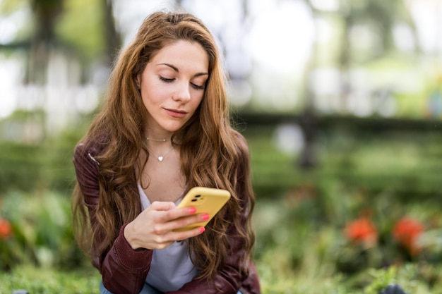 Giovane ragazza che guarda il suo smartphone seduta su una panchina nel formato parco con spazio copia da vicino