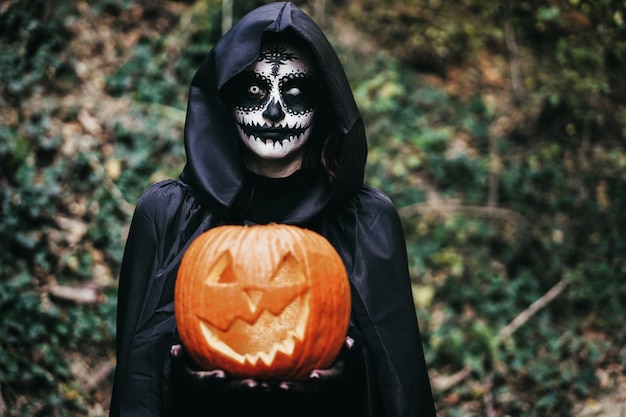 Giovane ragazza che indossa un misterioso abito di Halloween che tiene una zucca spaventosa - Focus on face