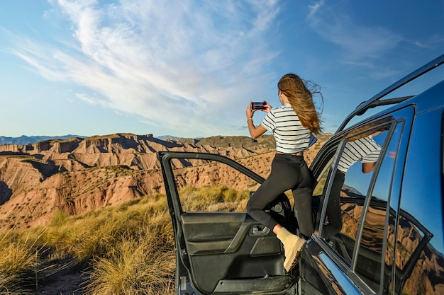 Giovane ragazza che scatta foto del paesaggio desertico attraverso il finestrino dell'auto