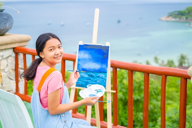 Giovane ragazza che utilizza un'immagine di disegno a pennello su carta di tela in una splendida vista del paesaggio a koh tao Thailandia