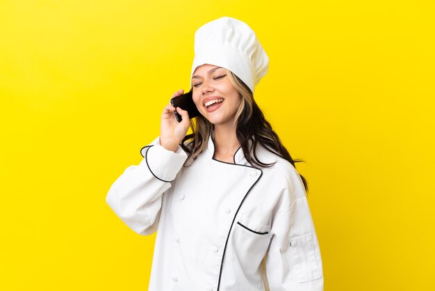 Giovane ragazza chef russa isolata su sfondo giallo che mantiene una conversazione con il telefono cellulare
