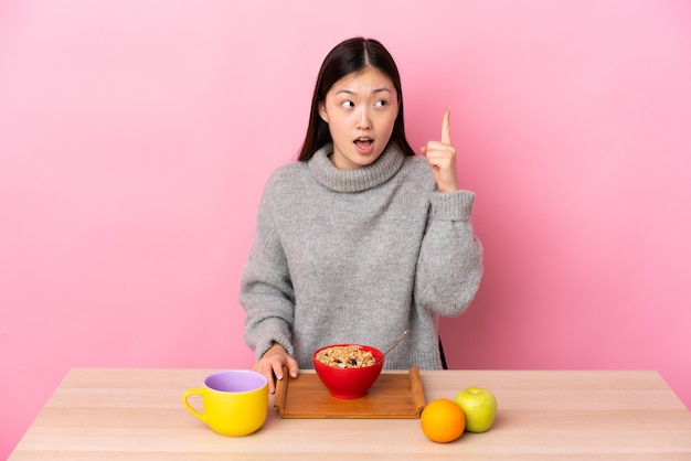 Giovane ragazza cinese che fa colazione in un tavolo che intende realizzare la soluzione sollevando un dito