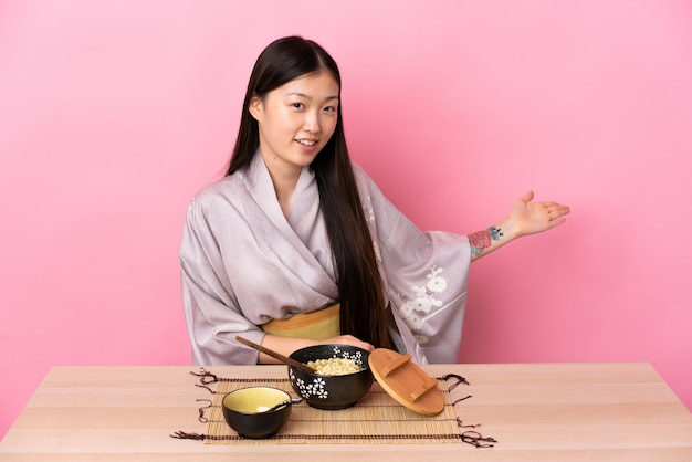 Giovane ragazza cinese che indossa un kimono e mangia noodles tendendo le mani a lato per invitare a venire