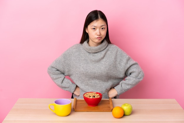 Giovane ragazza cinese che mangia prima colazione in una tabella arrabbiata