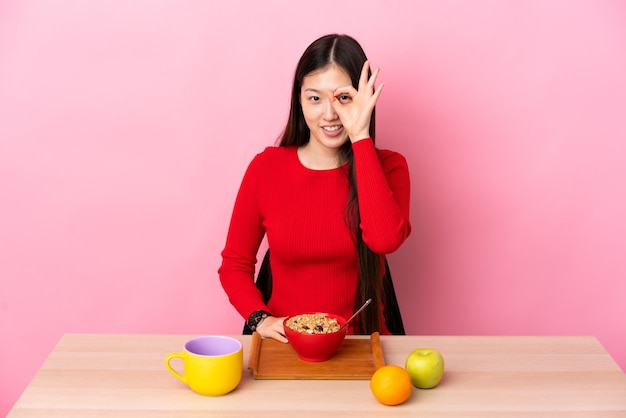 Giovane ragazza cinese che mangia prima colazione in una tabella che mostra segno giusto con le dita