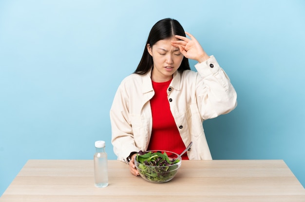 Giovane ragazza cinese che mangia un'insalata con espressione stanca e malata