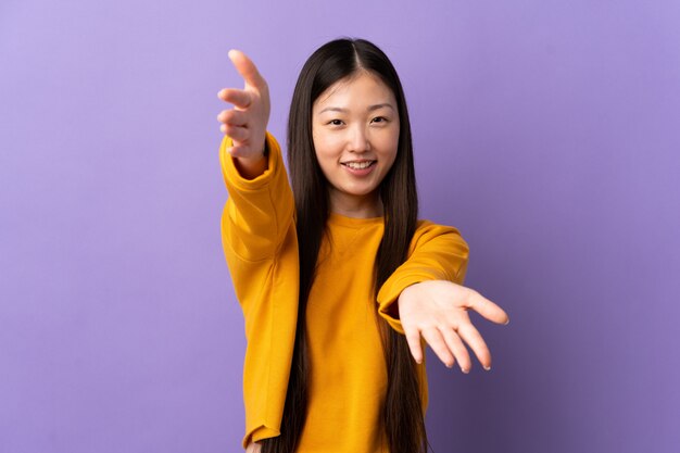 Giovane ragazza cinese sopra la parete viola che presenta e che invita a venire con la mano