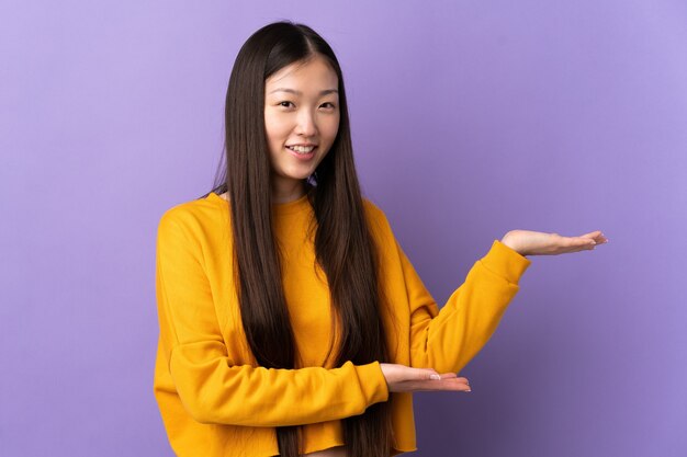 Giovane ragazza cinese sopra la parete viola isolata che estende le mani al lato per invitare a venire