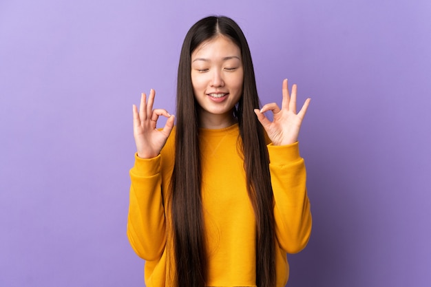 Giovane ragazza cinese sopra la parete viola isolata nella posa di zen