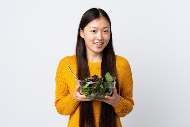 Giovane ragazza cinese su sfondo bianco isolato in possesso di una ciotola di insalata con felice espressione