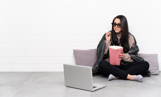 Giovane ragazza colombiana in una stanza con gli occhiali 3d e in possesso di un grande secchio di popcorn
