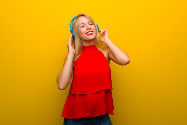 Giovane ragazza con abito rosso sulla parete gialla ascoltando musica con le cuffie