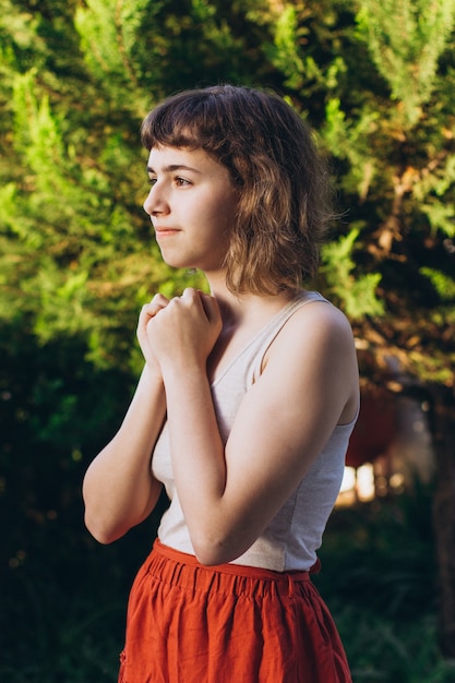 Giovane ragazza con capelli ricci corti che sorride con le mani vicino al viso. Bella ragazza adolescente fuori