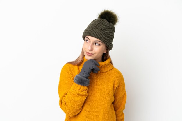 Giovane ragazza con cappello invernale isolato sul muro bianco e alzando lo sguardo