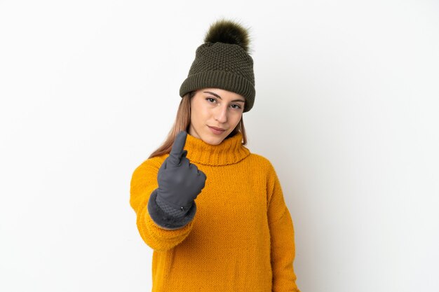 Giovane ragazza con cappello invernale isolato sul muro bianco facendo gesto in arrivo