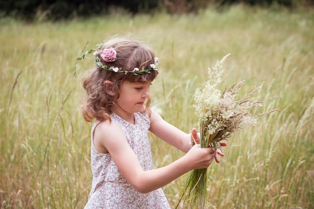 Giovane ragazza con fiori tra i capelli che raccoglie fiori selvatici in un prato