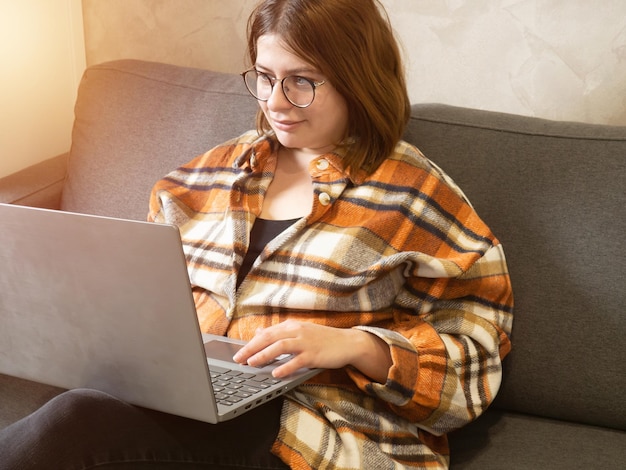 Giovane ragazza con gli occhiali che lavora su un computer portatile seduto a casa sul letto.