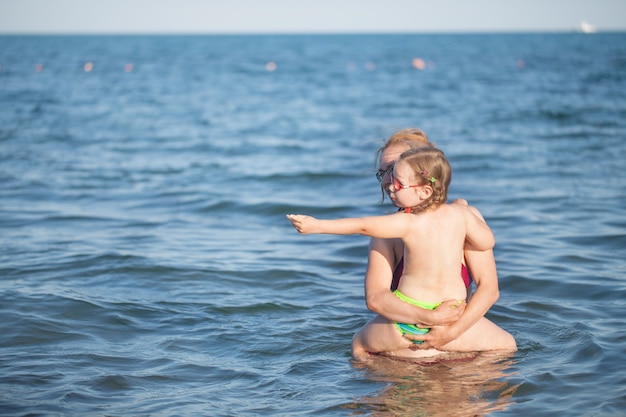 Giovane ragazza con gli occhiali rossi e un costume da bagno verde che riposa sul mare. infanzia e aria di mare