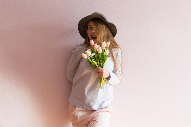 giovane ragazza con i capelli lunghi biondi sciolti un cappello di feltro in testa tiene i fiori di primavera nelle sue mani