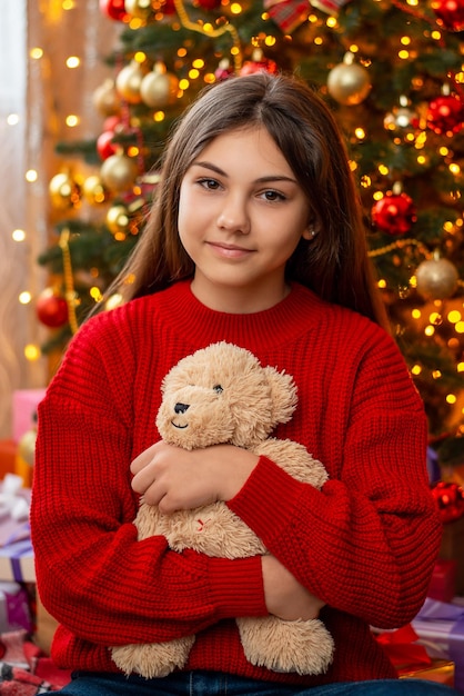 Giovane ragazza con i capelli lunghi in maglione rosso con orsacchiotto in mano Ritratto di una ragazza attraente in atmosfera natalizia