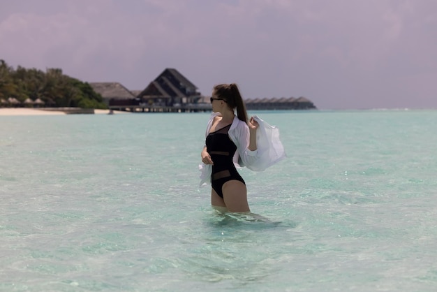 Giovane ragazza con i capelli lunghi in swinsuit nero e camicia bianca in turchese acqua blu menta dell'acqua