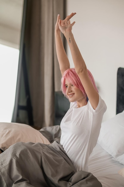 Giovane ragazza con i capelli rosa a letto che sembra assonnata