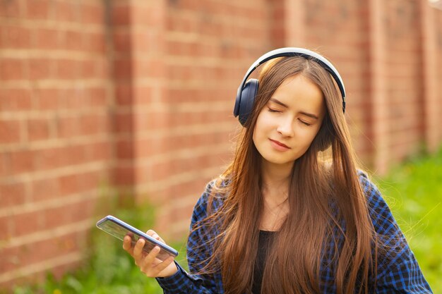 Giovane ragazza con le cuffie in giro per la città in estate, ascoltare musica, godersi, sorridere