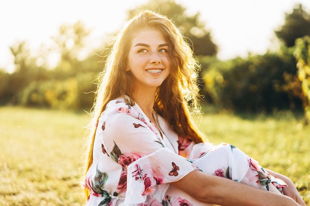 Giovane ragazza con lunghi capelli ricci, bruna, viso in lentiggini, con il trucco e gli occhi verdi, in posa vestito bianco chiaro