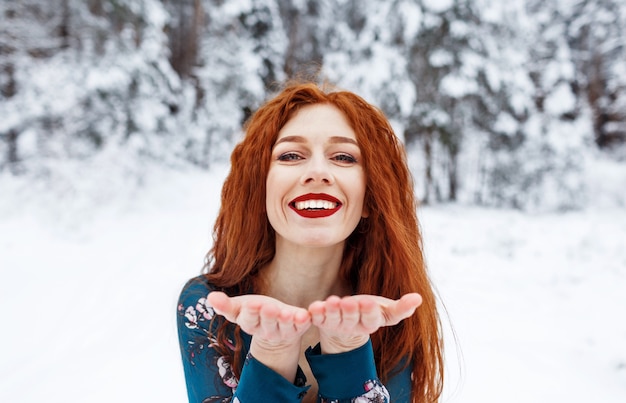 Giovane ragazza con lunghi capelli rossi in un abito estivo su un paesaggio invernale. Mandare un bacio