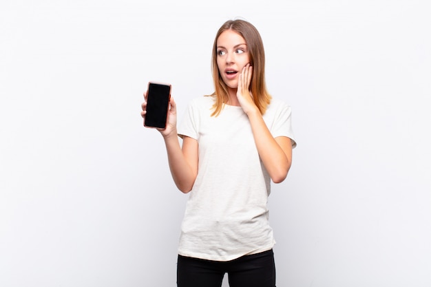 giovane ragazza con smartphone sorpreso guardando al lato con entrambe le mani sul viso