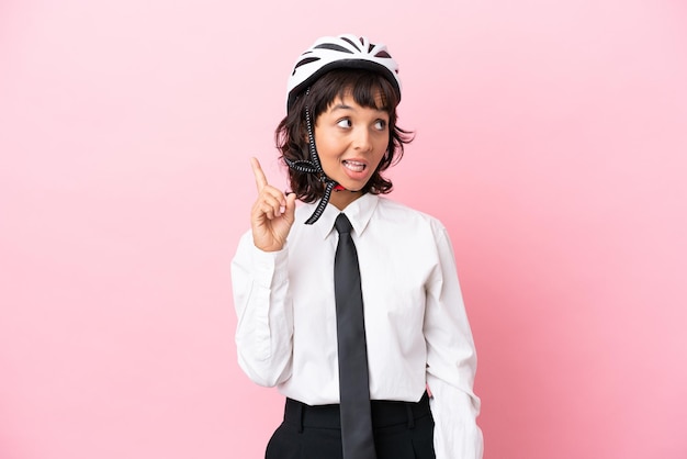 Giovane ragazza con un casco da bici isolato su sfondo rosa che intende realizzare la soluzione sollevando un dito
