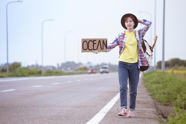 Giovane ragazza con una chitarra che arriva lungo la strada e fa l'autostop