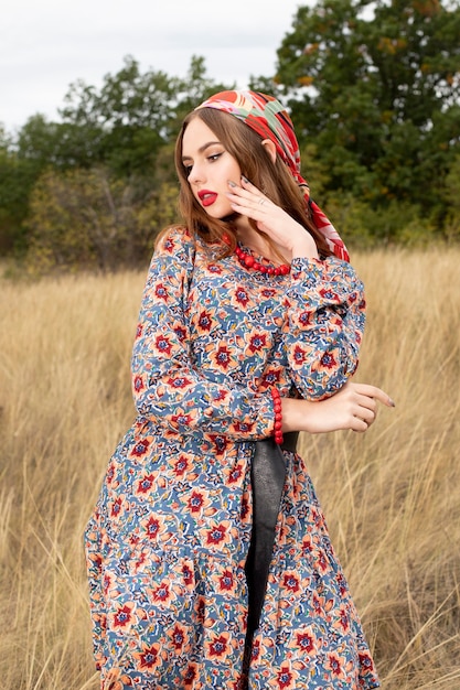 Giovane ragazza con una sciarpa in testa e un bel vestito in posa sullo sfondo della natura