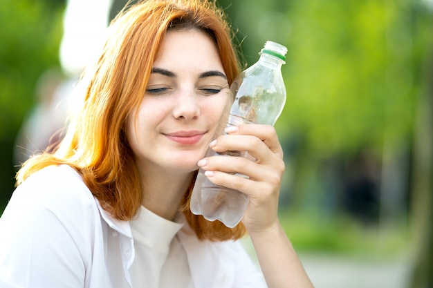 Giovane ragazza dai capelli rossi felice che tiene una bottiglia d'acqua