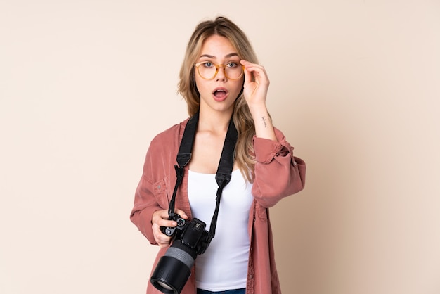 Giovane ragazza del fotografo sopra la parete isolata con i vetri e sorpresa