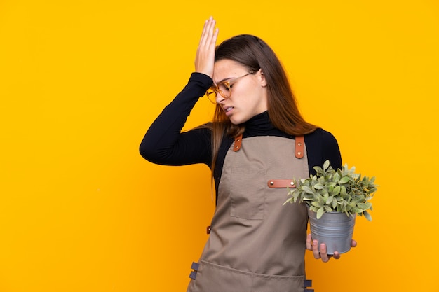 Giovane ragazza del giardiniere che tiene una pianta che ha dubbi con l'espressione confusa del fronte