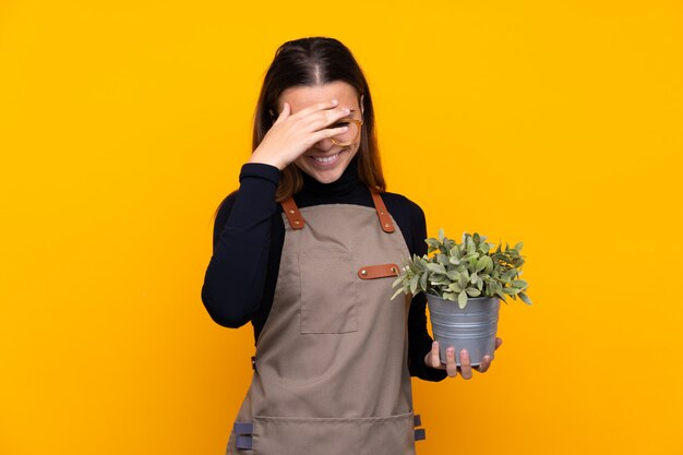 Giovane ragazza del giardiniere che tiene una pianta sopra la risata gialla isolata