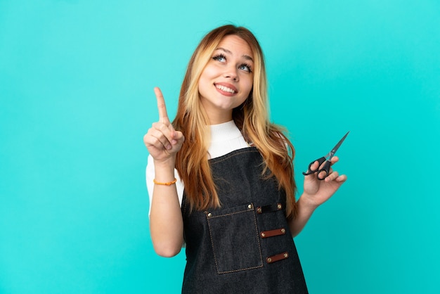 Giovane ragazza del parrucchiere sopra fondo blu isolato che indica su una grande idea