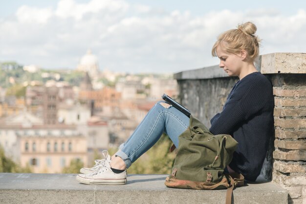 Giovane ragazza dello studente che legge un libro elettronico nel parco