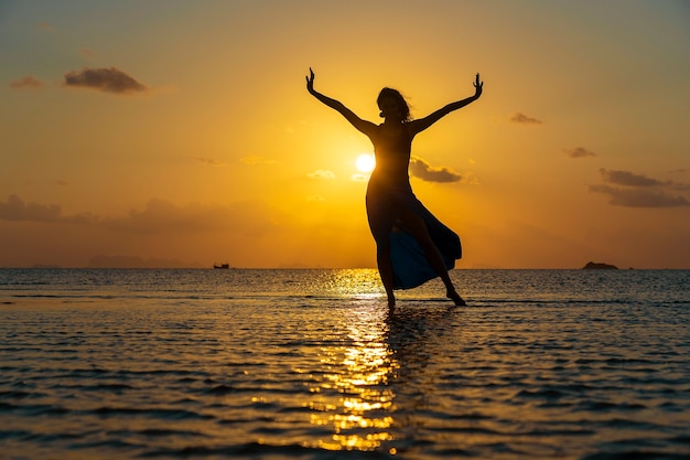 Giovane ragazza di bellezza che balla alla spiaggia tropicale sull'acqua di mare all'isola di paradiso al tramonto, si chiuda