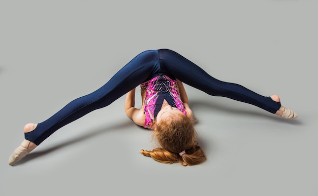Giovane ragazza di ginnastica elastica sdraiata sulla schiena con le gambe divise Ragazza sportiva che fa allungamento degli esercizi ginnici