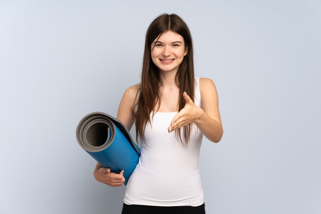 Giovane ragazza di sport che va alle lezioni di yoga mentre si tiene una stuoia che stringe la mano per chiudere un buon affare