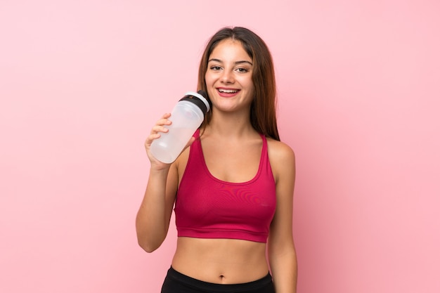 Giovane ragazza di sport sopra la parete rosa isolata con la bottiglia di acqua di sport