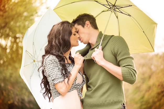 Giovane ragazza e un ragazzo in piedi che si abbracciano sotto gli ombrelloni e si baciano. Sullo sfondo c'è il verde.