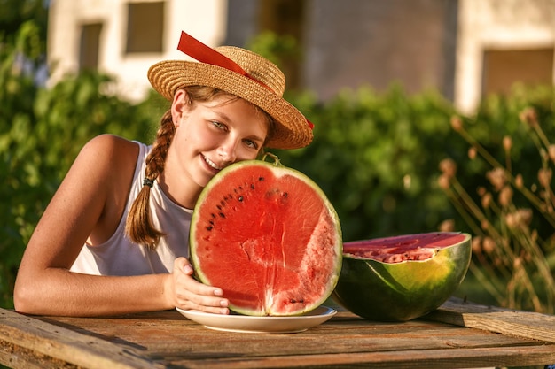 Giovane ragazza felice con cappello e metà di anguria fresca rossa godendo di una vita all'aria aperta. Adolescente che si gode la vita estiva.